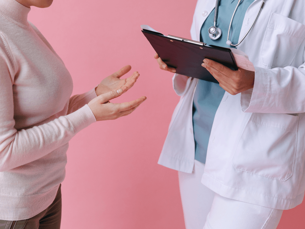 Close-up image of a doctor holding a board, with a stethoscope around their neck and a patient's hands non-verbally conversing