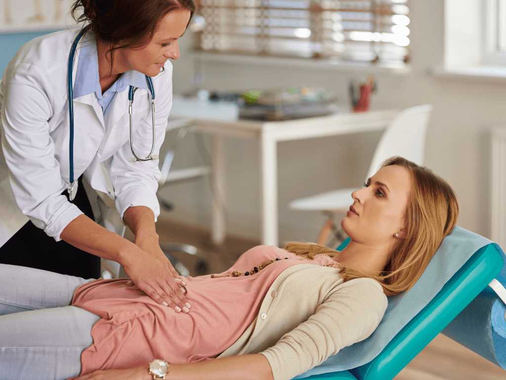 A female doctor pressing down on a woman's abdomen in an examination room