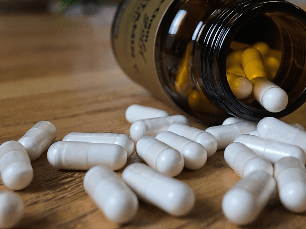 is-Chem Gold supplement bottle spilling white vegecapsules onto a wooden surface.
